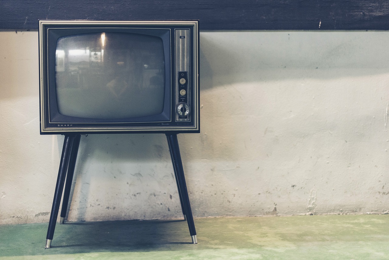 Old, vintage television on legs, set on a concrete floor.