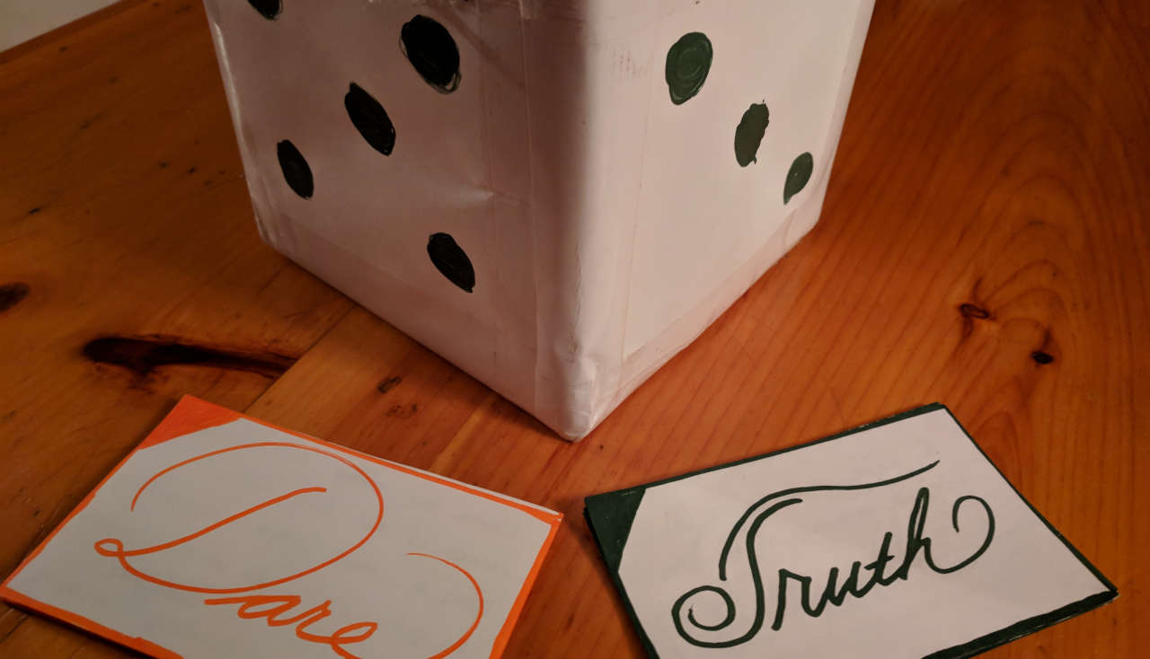 Cardboard paper dice with two index cards stacks, one reading ‘Dare’ and the other reading ‘Truth’.