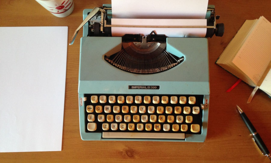 A blue typewriter, pen, and paper sitting on a desk.