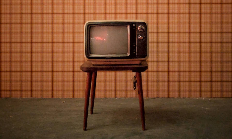 Old CRT TV sitting in front of a square-patterned wall.