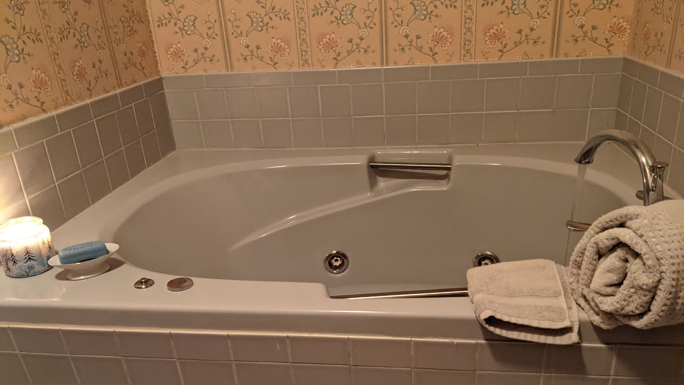 Whirlpool-style bathtub with blue-gray tile and step-up. 1980s-era wallpaper above.