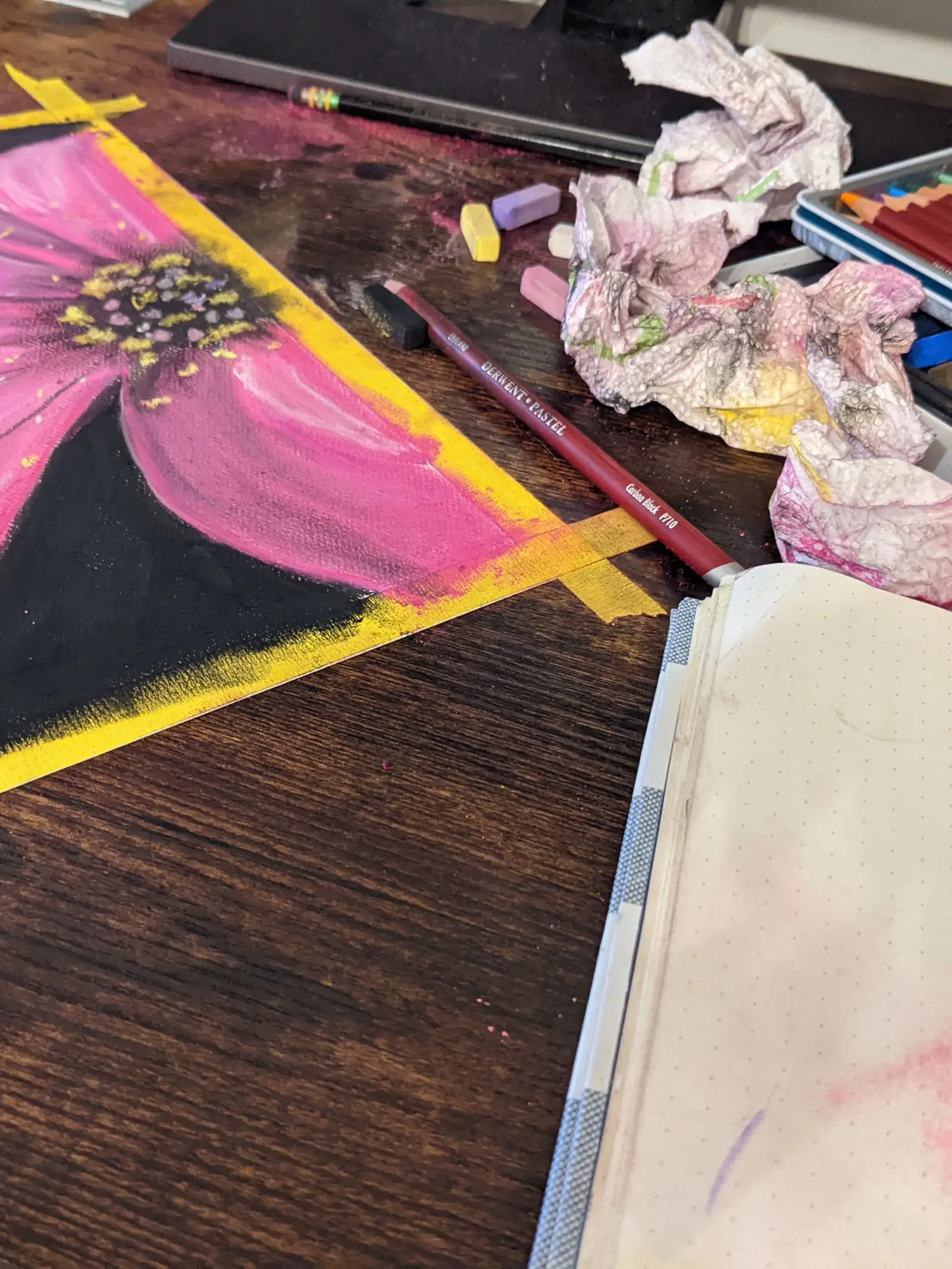 Pink daisy drawing taped to desk alongside pencils, pastels, and dirty paper towels.