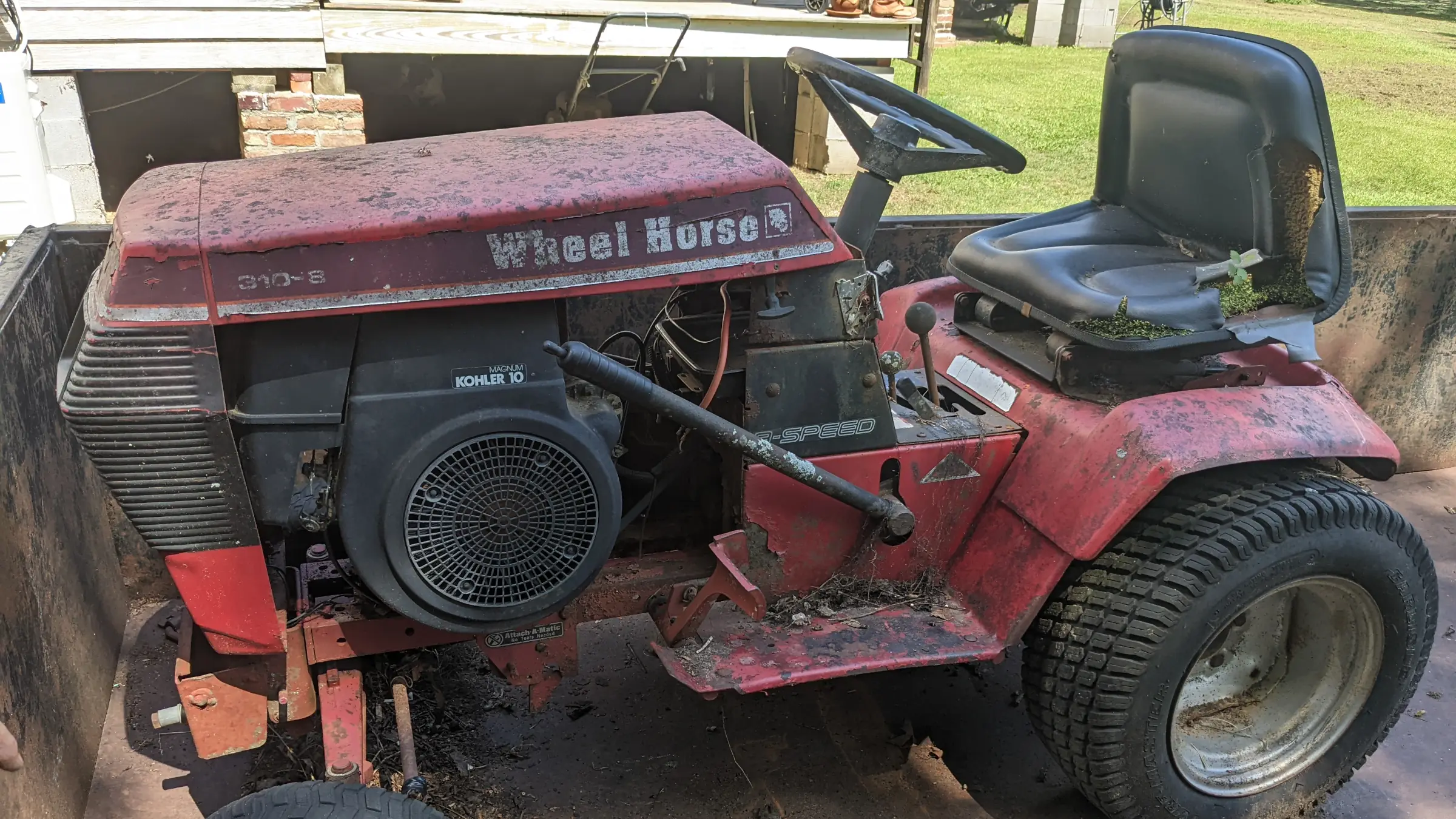 Old red riding lawn mower with peeling paint and rust sitting on a trailer bed.