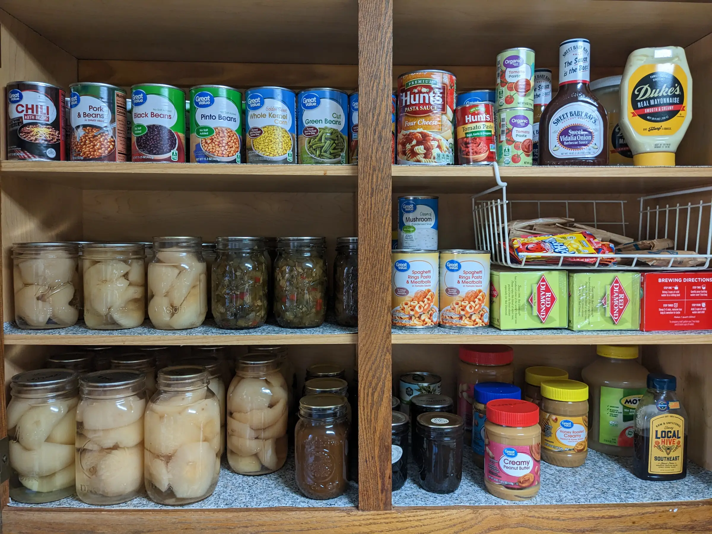 Wooden cabinet with three shelves of canned and jarred foods.