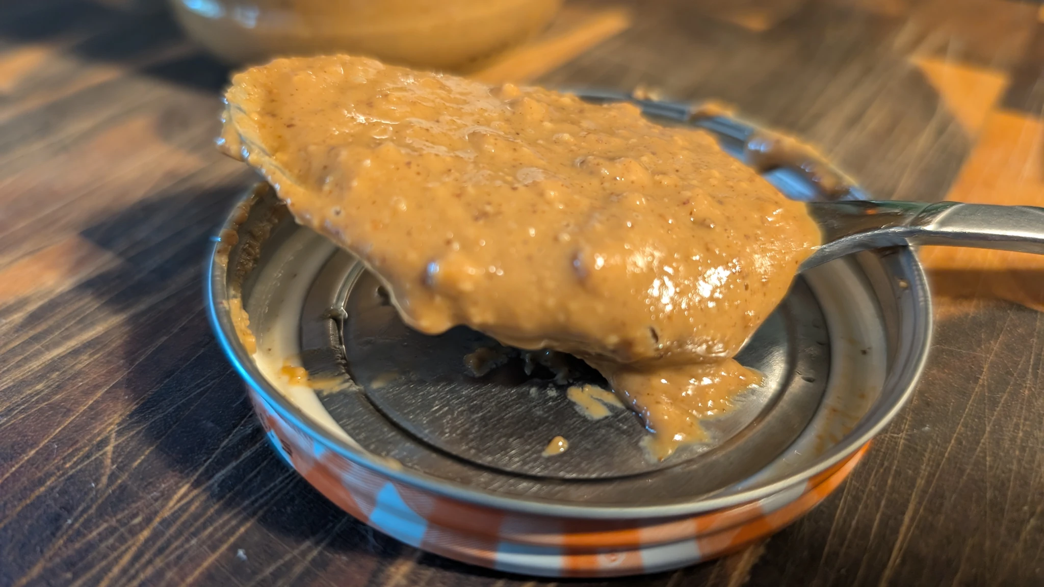 A spoonful of peanut butter sitting a jar lid.