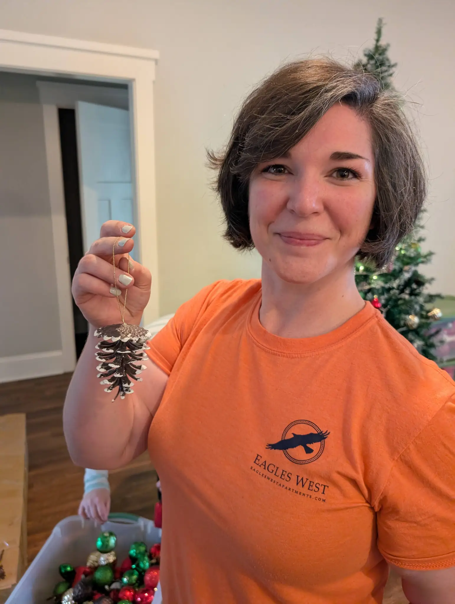 Ashley holding a pine comb ornament in front of a Christmas tree.