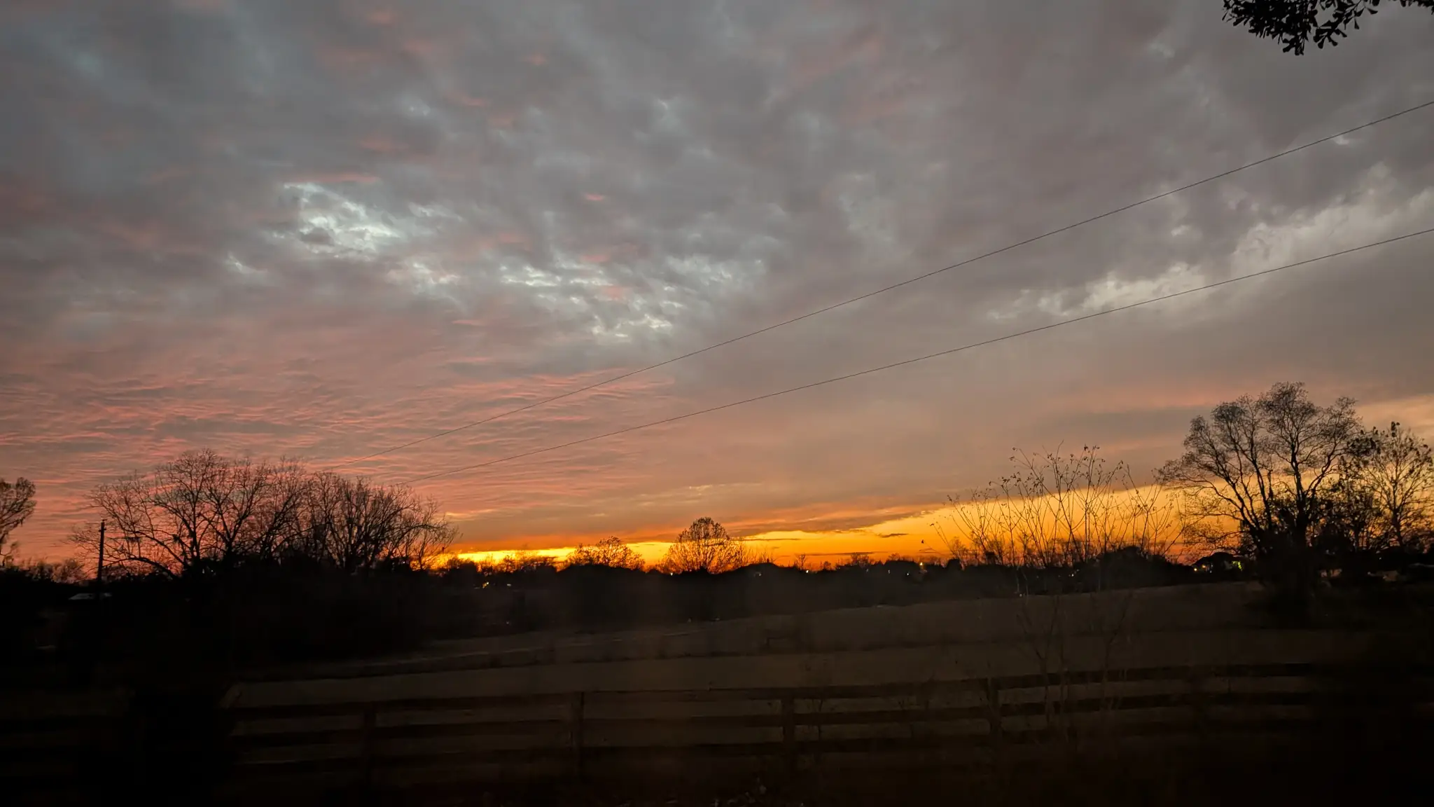 Orange sunset over a field with a fence in the foreground.